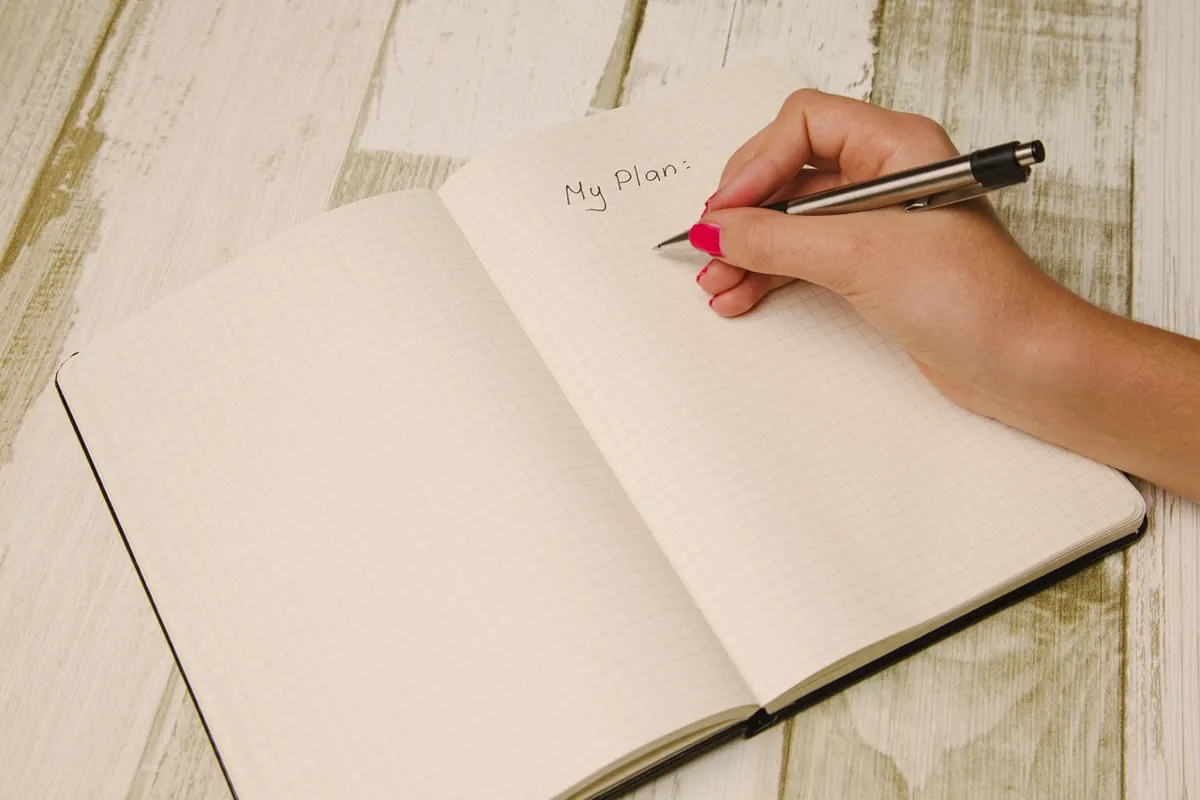 A person writing "My plan:" in a notebook. Writing in a notbook
