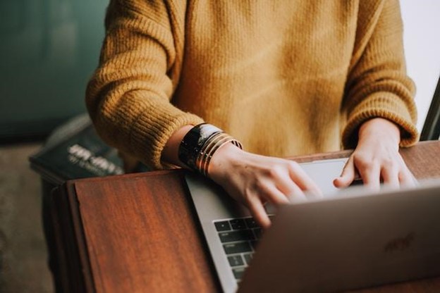 Person in a yellow sweater typing on a keyboard