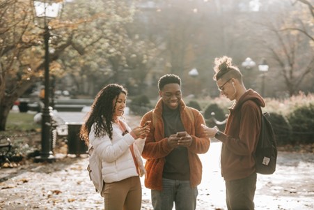 three friends in a park maintaining connections after a move using smartphones